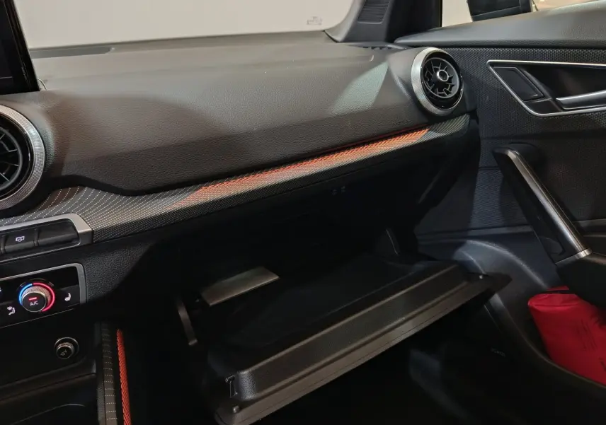 Intérieur côté passager de l'Audi Q2 35 TFSI noir, tableau de bord avec éclairage orange et boîte à gants ouverte.