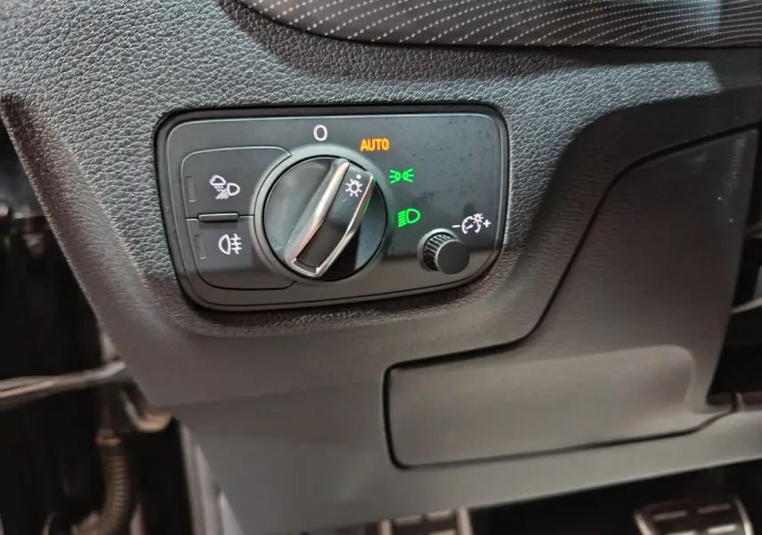 Gros plan sur le bouton de commande des phares avec réglage automatique dans l'Audi Q2 noir essence 2022 côté gauche.