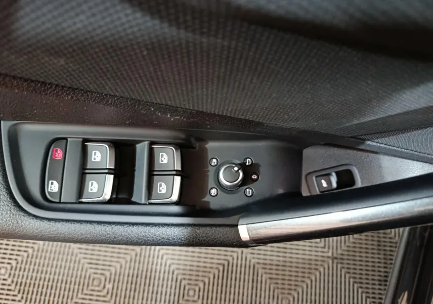 Gros plan sur la commande des vitres et rétroviseurs côté conducteur d'un Audi Q2 noir 2022, finition S Line Plus.