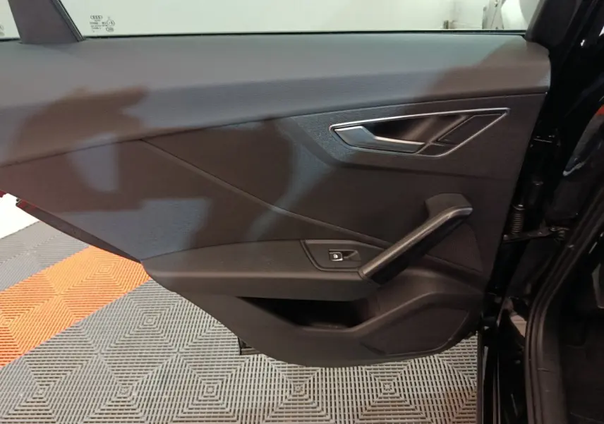 Vue rapprochée de la porte côté gauche noire de l'Audi Q2 35 TFSI 150 S Line Plus avec poignée et commande de vitre électrique.