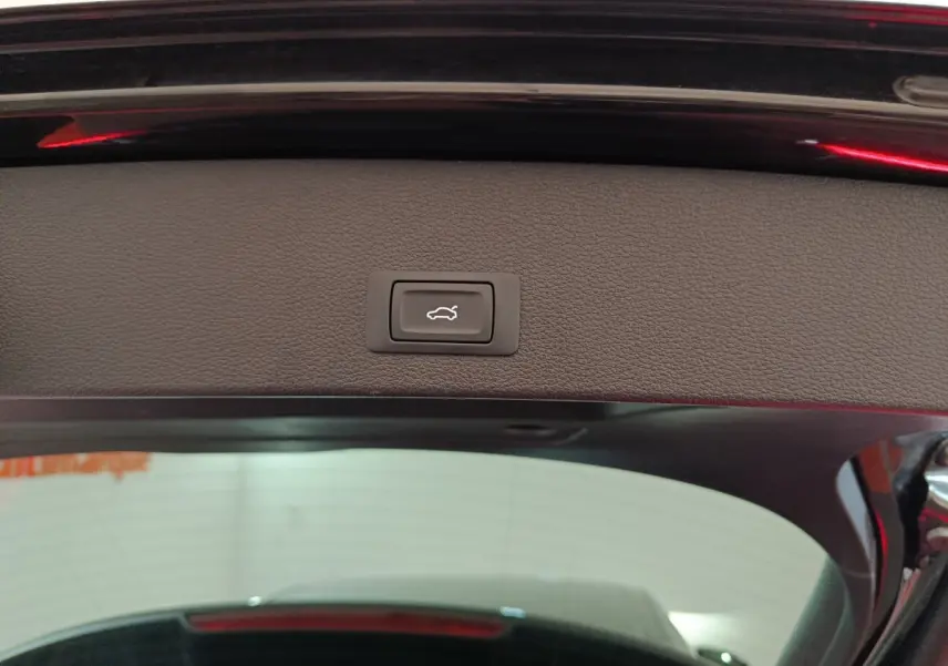 Bouton d'ouverture électrique du coffre sur le hayon intérieur d'un Audi Q2 noir, vue arrière rapprochée.
