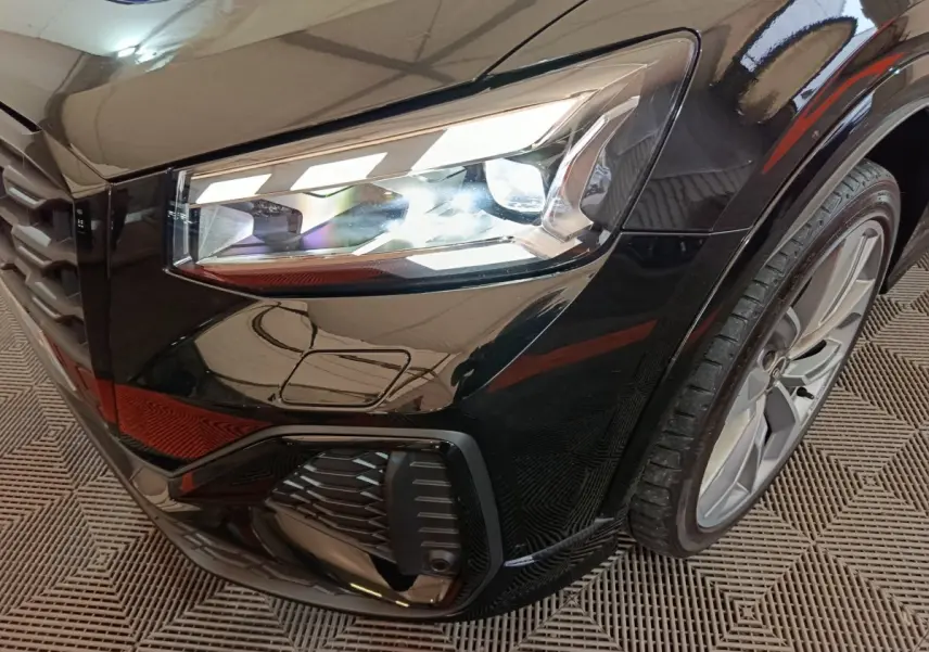 Gros plan sur le phare avant droit et la roue d'une Audi Q2 noire, finition S Line Plus, avec détails du pare-chocs.