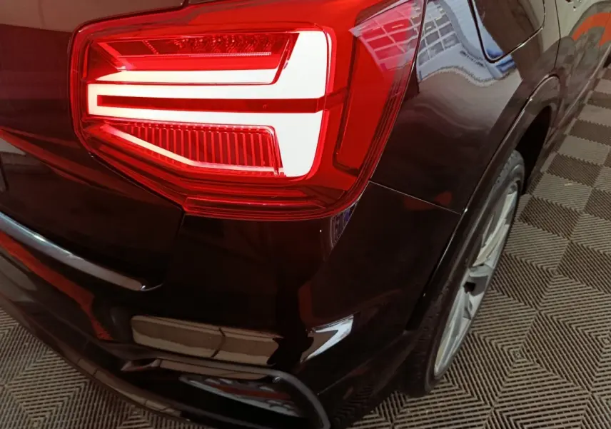 Gros plan sur le feu arrière gauche d'un Audi Q2 noir 2022, soulignant la finition S Line Plus et la jante arrière.