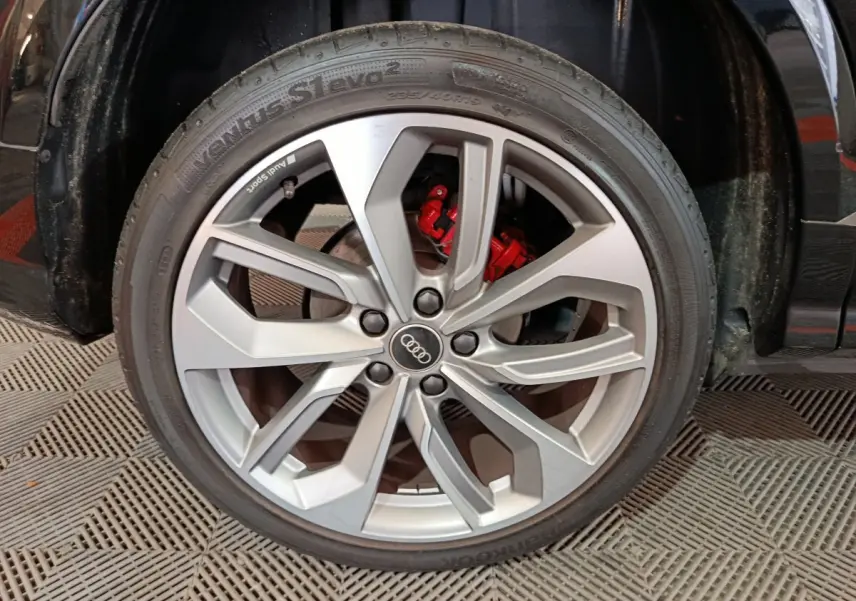 Gros plan sur la roue avant gauche d'un Audi Q2 noir, jante argentée à cinq doubles branches et étrier de frein rouge visible.