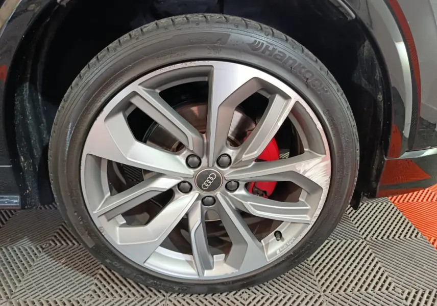 Gros plan sur la jante en alliage argentée avec logo Audi et étrier de frein rouge du côté avant droit d’un Audi Q2 noir.