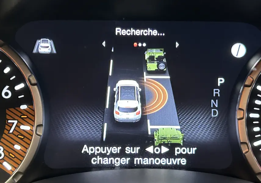 Affichage numérique du tableau de bord montrant l'assistance au stationnement avec vue du véhicule blanc en manœuvre.