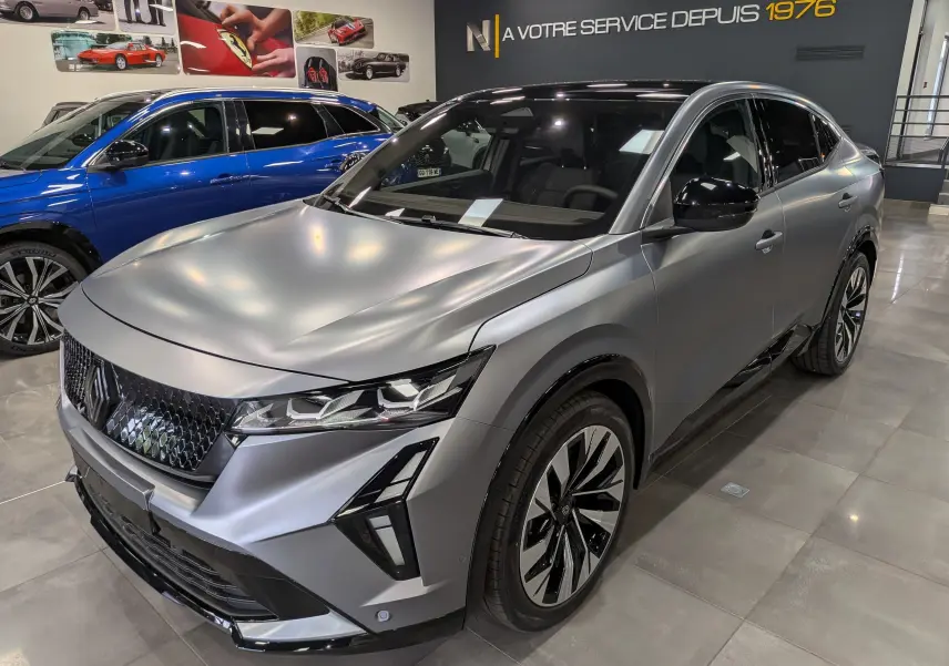 Renault Rafale E-Tech gris schiste satin en 3/4 avant droit, avec calandre noire et jantes bicolores en showroom.