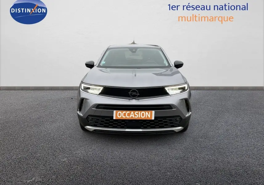 Vue frontale d'un Opel Mokka gris Artens métal avec phares allumés et plaque "OCCASION" visible.