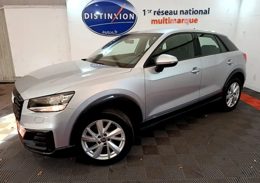 Audi Q2 35 TDI gris clair vue 3/4 avant droit en intérieur avec jantes alliage et phares allumés.