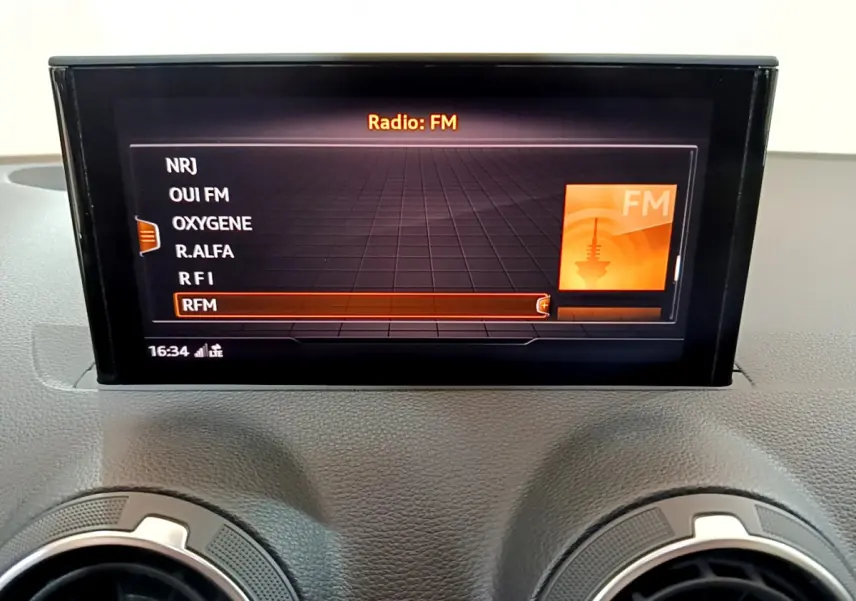 Écran central de l'Audi Q2 35 TDI 150 Design 2020 affichant les stations FM, avec aérateurs ronds en dessous.