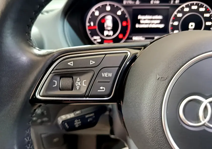 Gros plan sur le volant cuir noir de l'Audi Q2 35 TDI 150 Design avec commandes multifonctions et tableau de bord numérique.