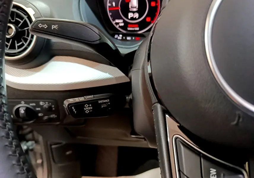 Gros plan sur le volant cuir et commandes au volant côté gauche de l’Audi Q2 35 TDI 150 Design gris clair, avec tableau de bord numérique.