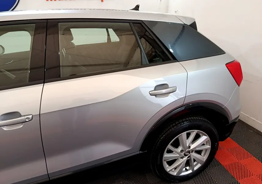 Vue latérale droite sur l'arrière d'un Audi Q2 gris clair, avec jante alliage et vitre arrière teintée.