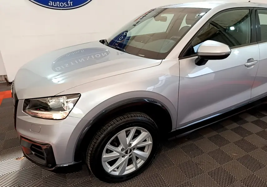 Vue 3/4 avant droit d'un Audi Q2 gris clair avec jantes alliage et rétroviseur argenté en intérieur showroom.