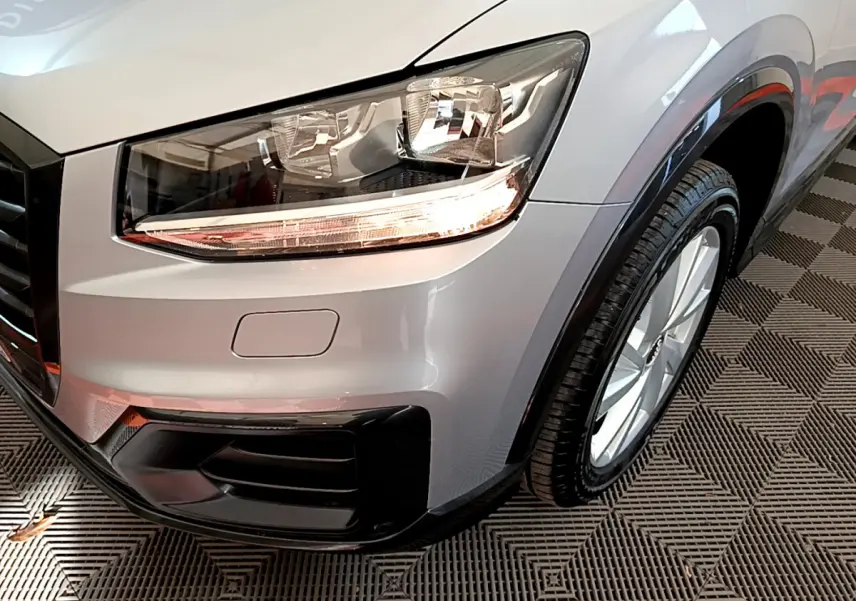 Gros plan sur l'avant droit gris clair de l'Audi Q2 35 TDI 150 Design, mettant en valeur le phare et la roue.