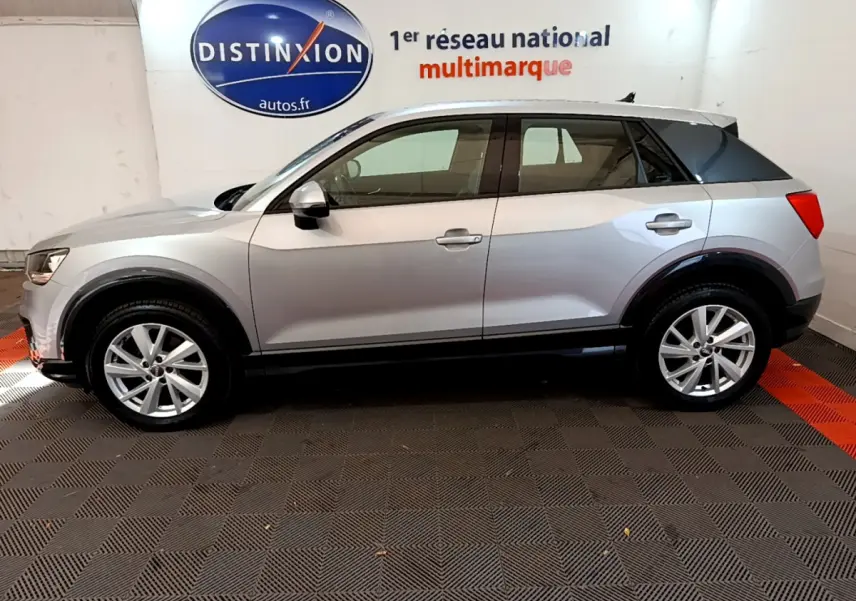 Audi Q2 35 TDI 150 Design gris clair vue de profil côté gauche dans un showroom avec logo Distinxion en arrière-plan.
