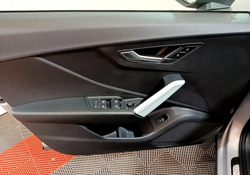 Vue intérieure du panneau de porte côté conducteur de l'Audi Q2 gris clair avec commandes de vitres et poignée argentée.