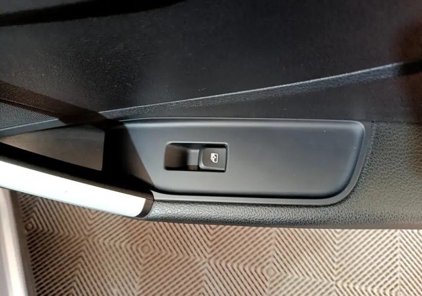 Bouton de commande de vitre électrique sur la porte côté conducteur d'un Audi Q2 gris clair, vue rapprochée.