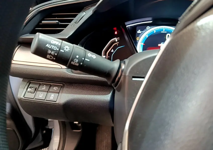 Vue rapprochée du commodo d'éclairage et du tableau de bord numérique de la Honda Civic 1.0 i-VTEC gris foncé.