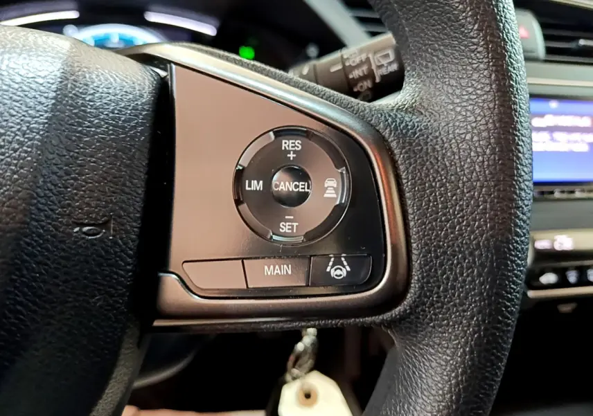 Gros plan sur les commandes du régulateur de vitesse au volant cuir noir d'une Honda Civic gris foncé 2020.
