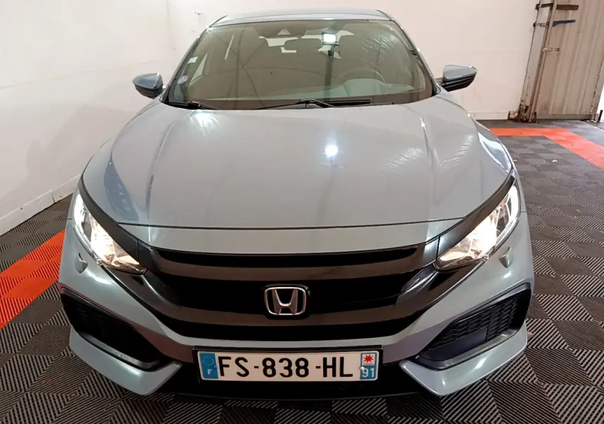 Vue frontale d'une Honda Civic gris foncé avec phares allumés et calandre noire brillante dans un garage.
