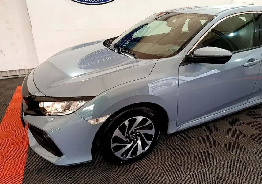 Vue 3/4 avant droit d'une Honda Civic 1.0 i-VTEC Exclusive gris foncé avec jantes alliage et phares allumés.