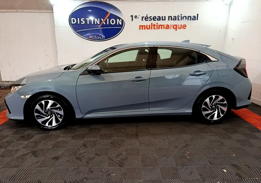 Profil côté gauche d'une Honda Civic 1.0 i-VTEC Exclusive gris foncé, avec jantes alliage et vitres teintées, en intérieur showroom.