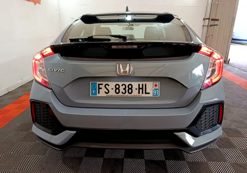 Vue arrière d'une Honda Civic gris foncé 2020 avec feux arrière allumés et aileron noir distinctif.