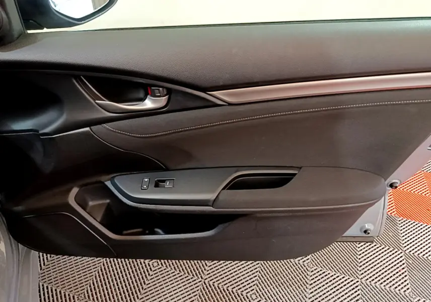Vue intérieure du panneau de porte côté droit de la Honda Civic 1.0 i-VTEC Exclusive gris foncé, avec poignée métallique et commandes vitres.