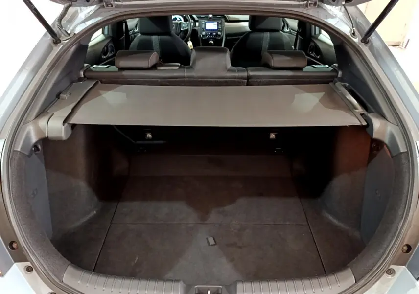 Vue intérieure du coffre ouvert d'une Honda Civic gris foncé, avec tablette cache-bagages et sièges arrière visibles.