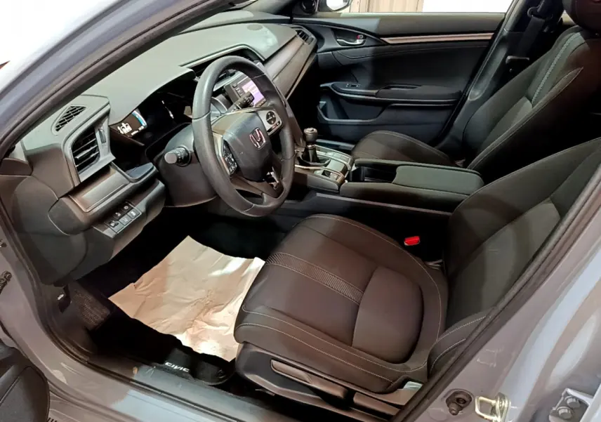 Vue intérieure côté conducteur de la Honda Civic 1.0 i-VTEC Exclusive 2020 avec sièges noirs et volant cuir multifonctions.