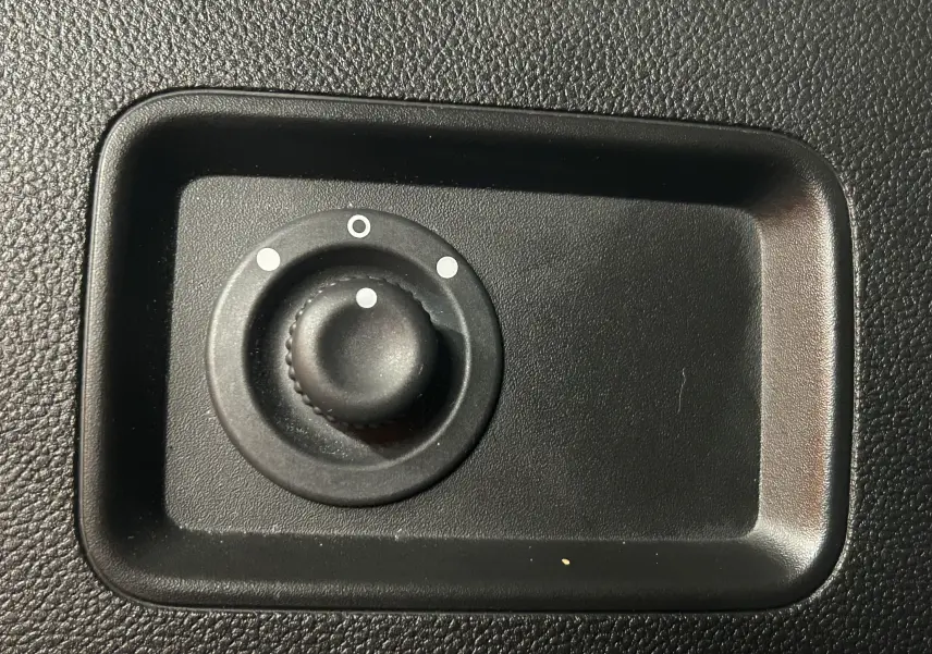 Bouton rotatif noir de réglage des rétroviseurs sur panneau intérieur texturé, détail du Dacia Duster 2024.