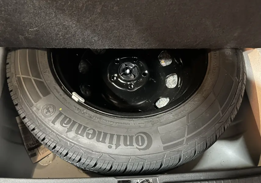 Gros plan sur la roue de secours Continental noire, logée dans le coffre du Dacia Duster blanc 2024.