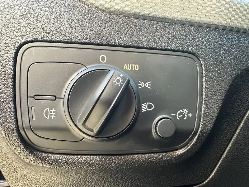 Gros plan sur le sélecteur de phares noir dans l'habitacle de l'Audi Q2 blanc 2023, version S line.
