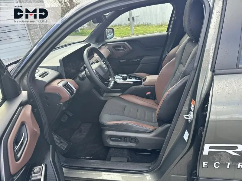 Vue côté gauche de l'intérieur du Suzuki Vitara 2026, sièges tissu/cuir marron et noir avec tableau de bord assorti.