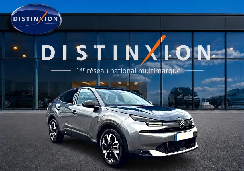 Citroën C4 X gris mercure vue 3/4 avant droit, avec jantes alu et calandre distinctive devant un showroom Distinxion.
