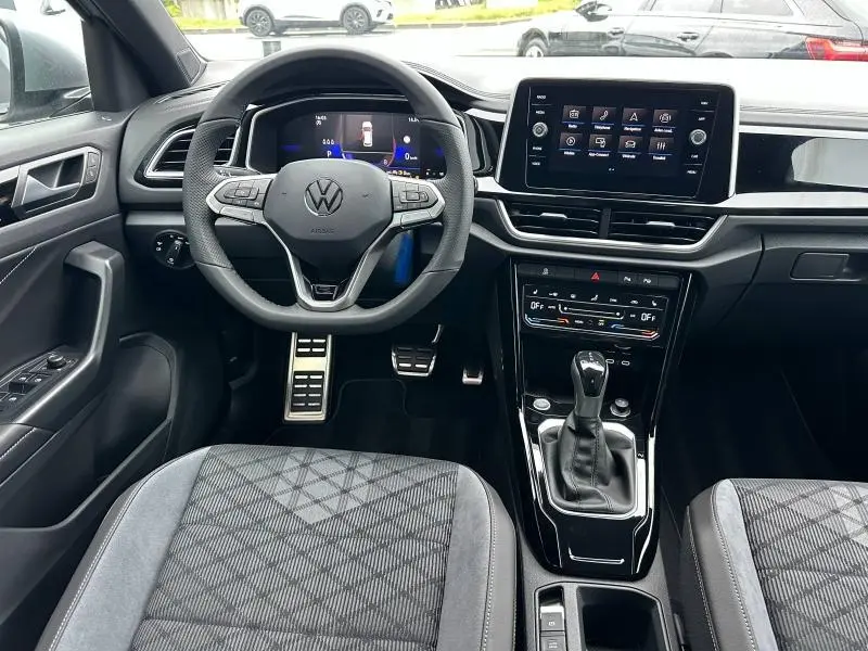 Intérieur du Volkswagen T-Roc gris 2025, vue frontale du poste de conduite avec volant multifonction et écran tactile central.