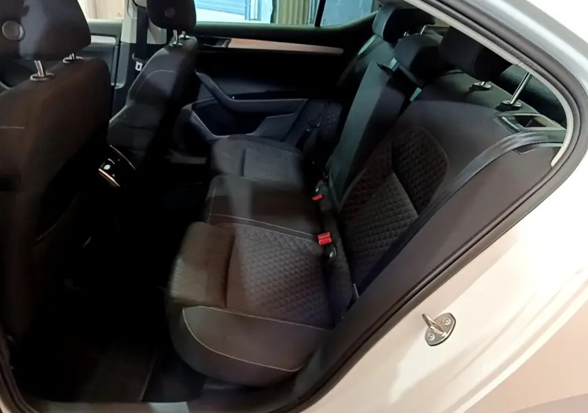 Vue intérieure côté droit sur la banquette arrière noire matelassée d’une Skoda Superb blanche, porte ouverte.