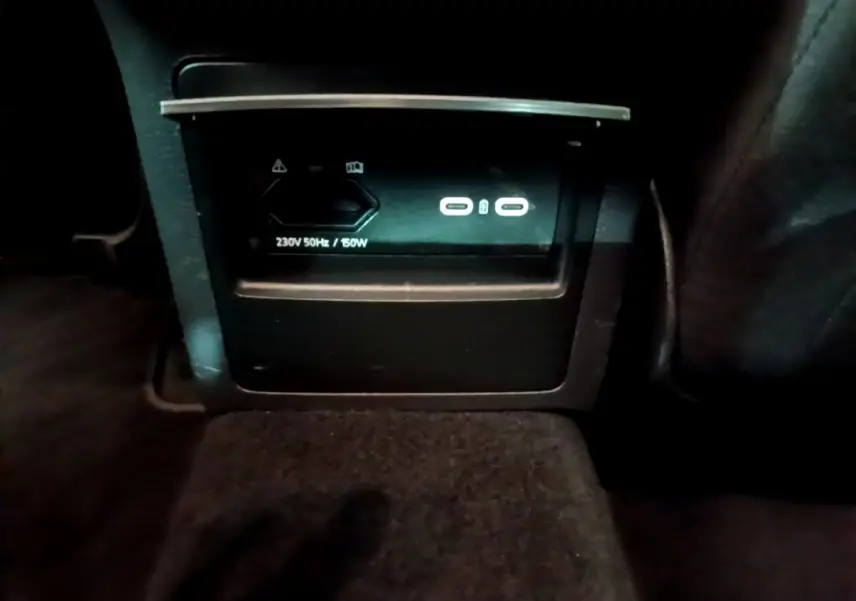 Prise électrique 230V et ports USB visibles à l'arrière de la console centrale d'une Skoda Superb blanche.