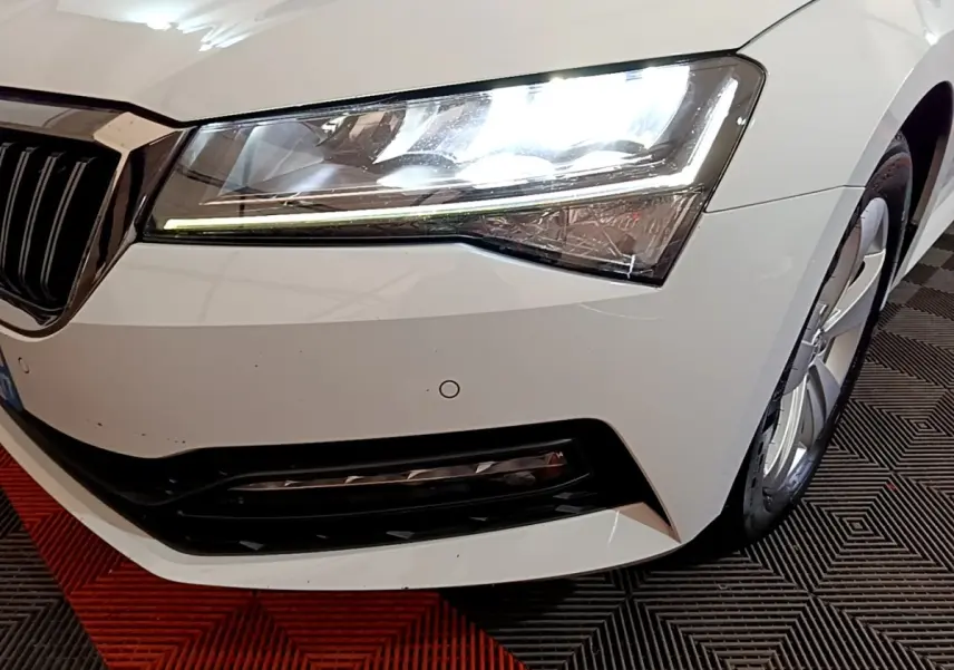 Gros plan sur l'avant droit blanc d'une Skoda Superb 2021, mettant en valeur le phare LED et la calandre noire.
