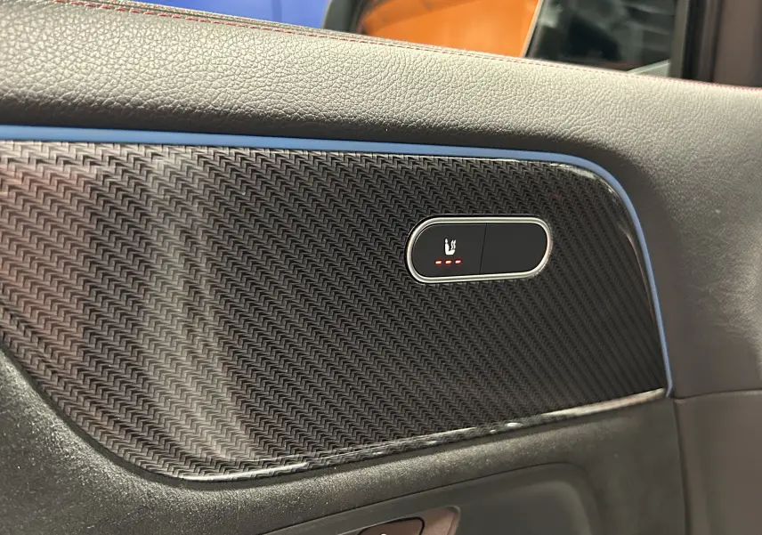 Détail du panneau de porte côté gauche en carbone avec bouton de siège chauffant illuminé sur Mercedes GLA 200 D AMG Line 2024.