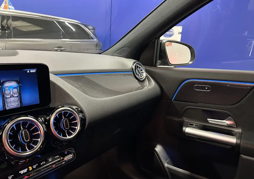 Intérieur avant droit de la Mercedes GLA 200 D AMG Line 2024 avec éclairage d'ambiance bleu et finitions carbone.