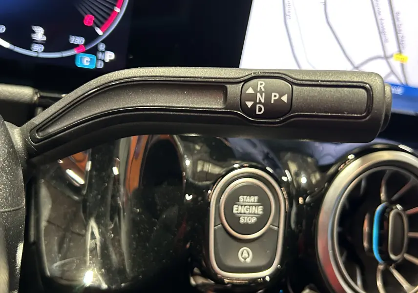 Gros plan sur la commande de boîte automatique et bouton start/stop du tableau de bord noir brillant d'une Mercedes GLA 200 D AMG Line 2024.