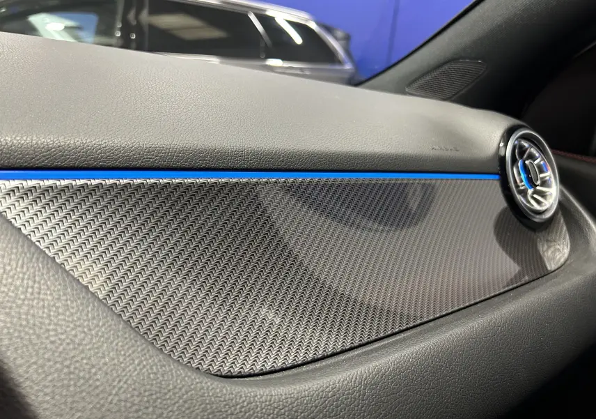 Détail de la planche de bord en carbone avec éclairage bleu d’ambiance dans le Mercedes GLA 200 D AMG Line 2024.
