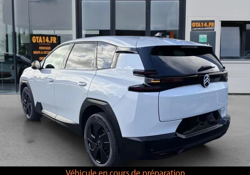 Vue 3/4 arrière droite d’un Citroën C5 Aircross hybride blanc avec toit noir et jantes noires devant un bâtiment.
