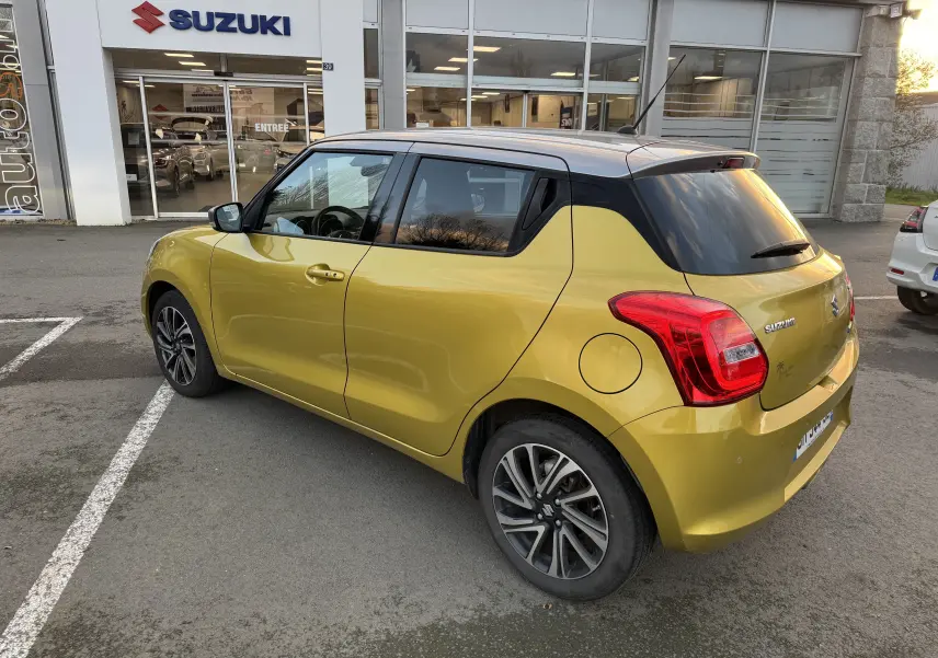 Suzuki Swift 1.2 Pack Auto hybride essence jaune et gris vue 3/4 arrière droit sur parking devant concession.