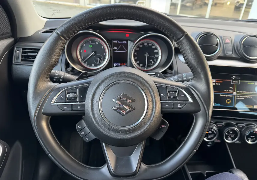 Vue rapprochée du volant noir de la Suzuki Swift 1.2 Pack Auto 2023 avec tableau de bord et écran tactile visibles.