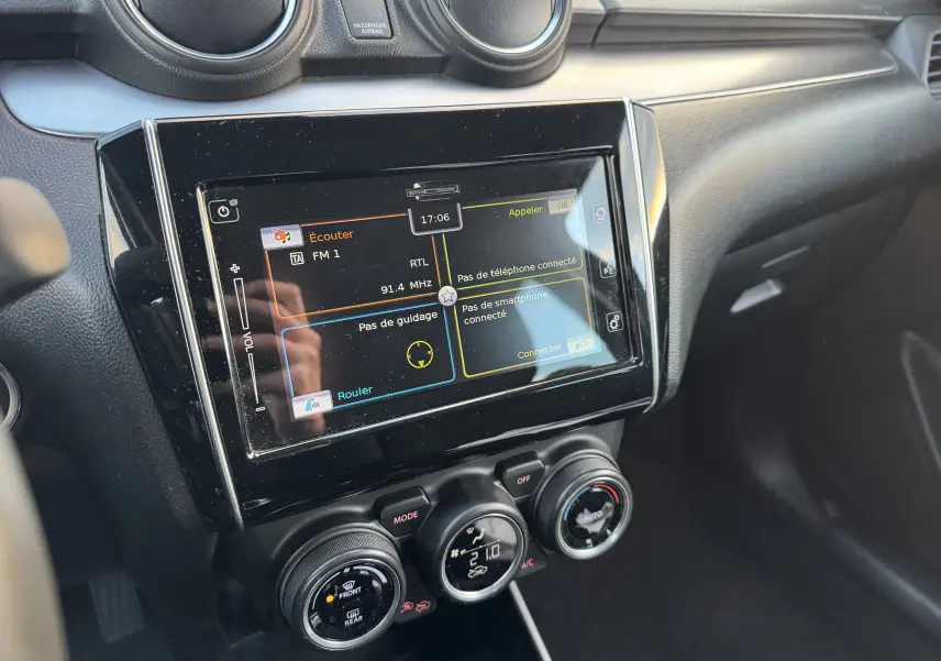 Vue rapprochée de la console centrale noire de la Suzuki Swift 1.2 Pack Auto 2023 avec écran tactile et commandes de climatisation.