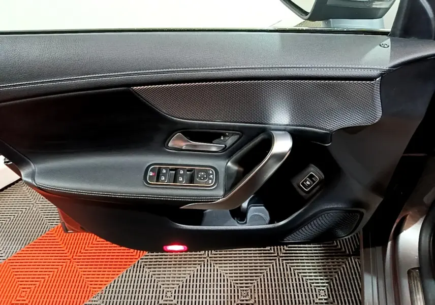 Vue rapprochée de la porte intérieure côté conducteur noire avec commandes électriques et poignée argentée d’une Mercedes CLA 180 d 2021.