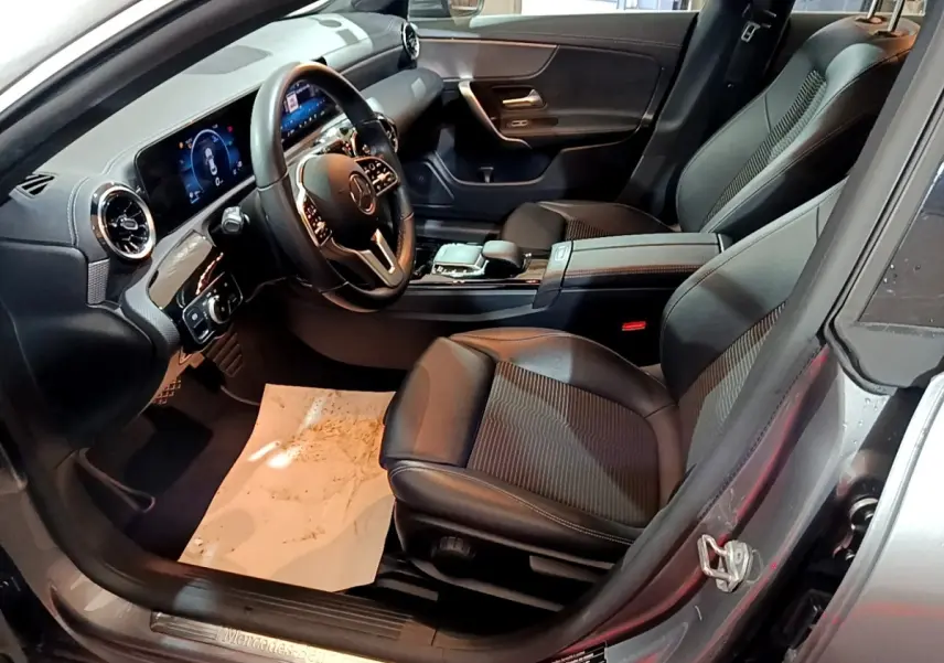 Vue intérieure côté conducteur de la Mercedes CLA 180 d Business Line 2021 gris clair, avec tableau de bord numérique et sièges en cuir noir.